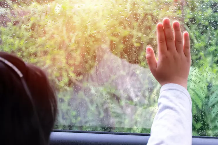 เด็กผู้หญิงนั่งมองน้ำฝนที่ตกลงมาบนกระจกรถ 