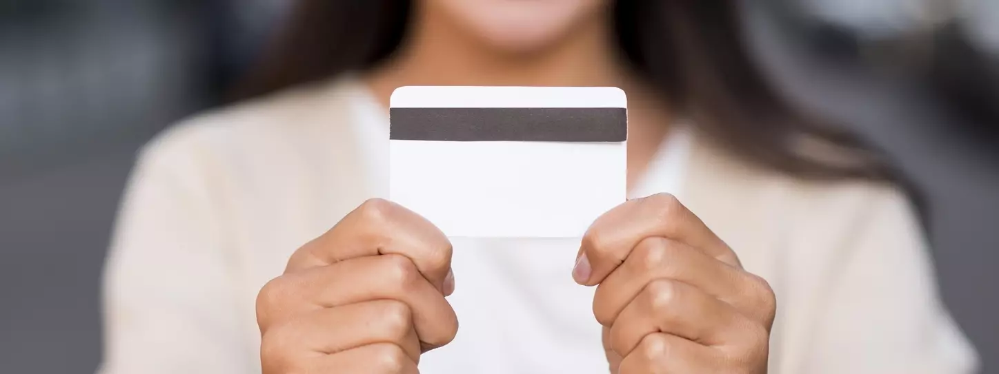 ผู้หญิงยืนยิ้มและถือบัตรเครดิตในมือ