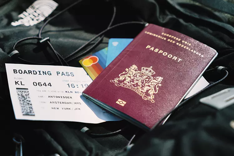 หนังสือเดินทางวางอยู่บนบัตรเครดิต ตั๋วเครื่องบิน และกระเป๋าสีดำ 