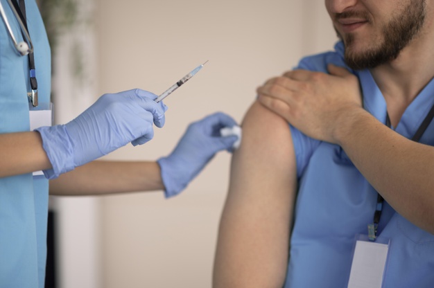 หมอถือเข็มฉีดยากำลังเตรียมฉีดวัคซีนบริเวณต้นแขนของผู้ชาย