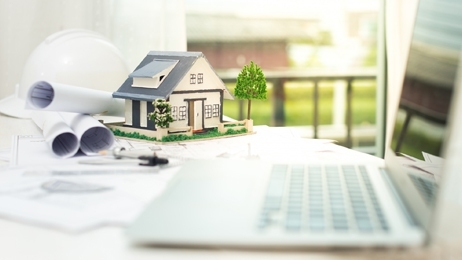 แบบแปลนบ้าน โมเดลบ้าน และโน๊ตบุ๊ควางอยู่บนโต๊ะ