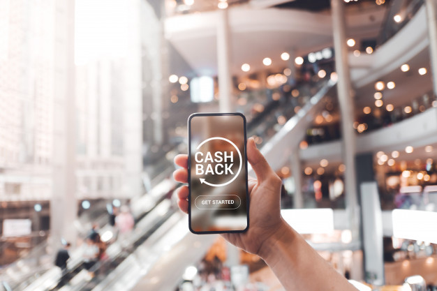 คนถือโทรศัพท์ที่มีคำว่า Cashback พร้อมด้านหลังเป็นห้างสรรพสินค้า