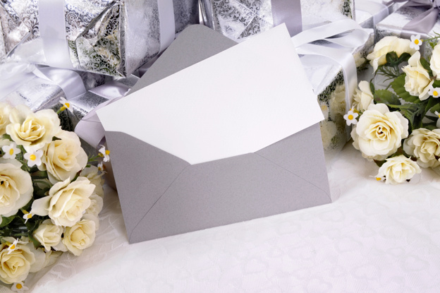 ซองสีเทาและการ์ดวางอยู่กับกล่องของขวัญและดอกกุหลาบสีขาว 