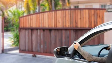 ผู้หญิงเปิดหน้าต่างรถและใช้รีโมทเปิดประตูรั้วบ้าน