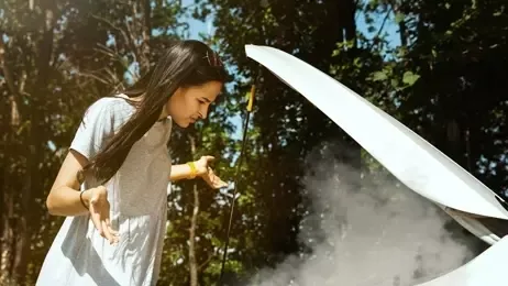 ผู้หญิงยืนอยู่หน้าฝากระโปรงรถยนต์ที่มีควันสีขาวพุ่งออกมา