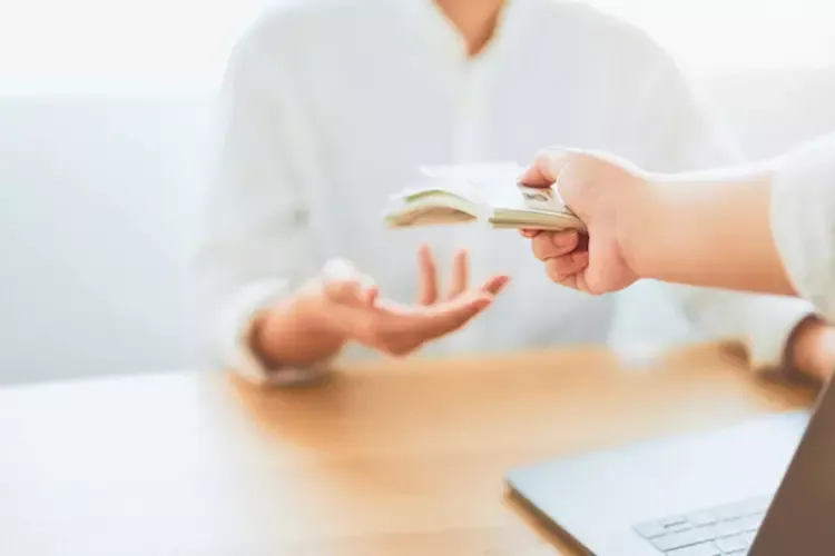 ผู้ชายกำลังยื่นธนบัตรให้คนที่นั่งฝั่งตรงข้าม 