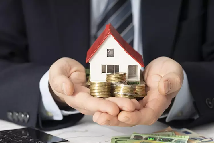 ผู้ชายถือโมเดลบ้านและเหรียญบนมือ 