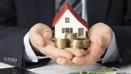 นักธุรกิจถือโมเดลบ้านและกองเหรียญบนมือ