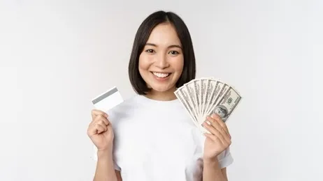 ผู้หญิงยืนถือบัตรกดเงินสดและธนบัตรในมือ