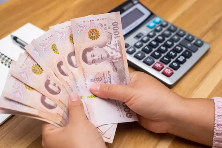 ผู้หญิงถือธนบัตรใบละ 1,000 บาท ไว้ในมือ 