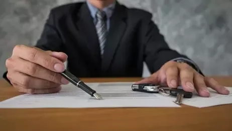 นักธุรกิจเอาปากกาชี้ที่เอกสาร และด้านข้างมีกุญแจรถวางอยู่