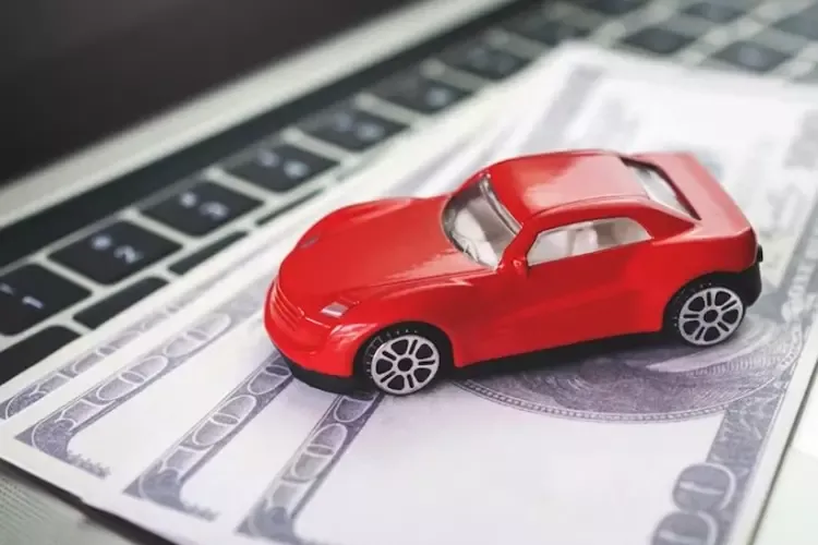 โมเดลรถสีแดงวางบนธนบัตรที่อยู่บนโน้ตบุ๊ก 