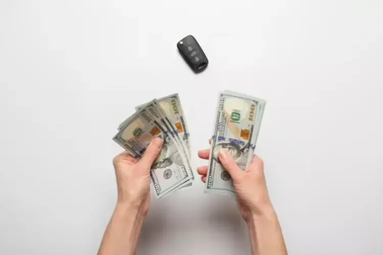 คนกำลังนับเงินดอลลาร์และมีกุญแจรถวางบนโต๊ะ 