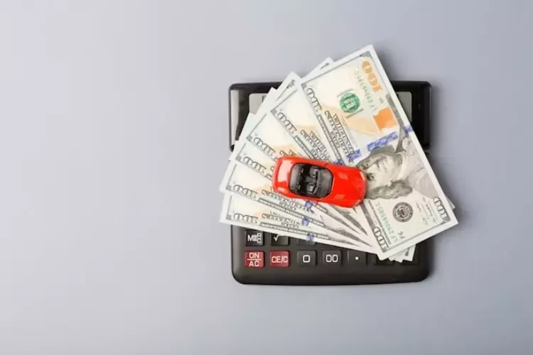 รถสีแดงวางบนเครื่องคิดเลขและกองเงินดอลลาร์ 