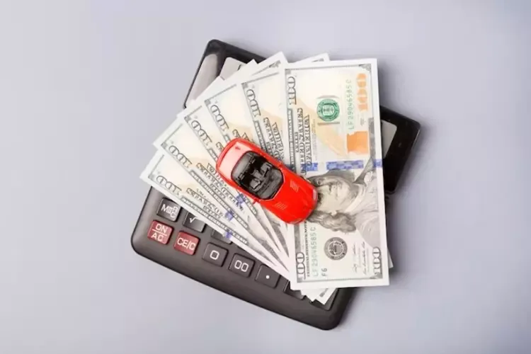 รถสีแดงคันเล็กวางบนเครื่องคิดเลขและกองเงินดอลลาร์ รถสีแดงคันเล็กวางบนเครื่องคิดเลขและกองเงินดอลลาร์