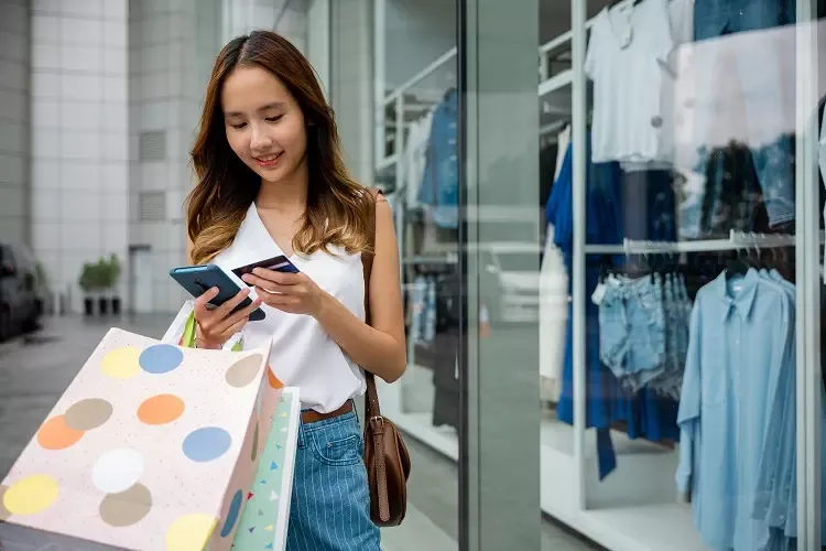 ผู้หญิงถือถุงช้อปปิ้งพร้อมโทรศัพท์มือถือและบัตรเครดิต