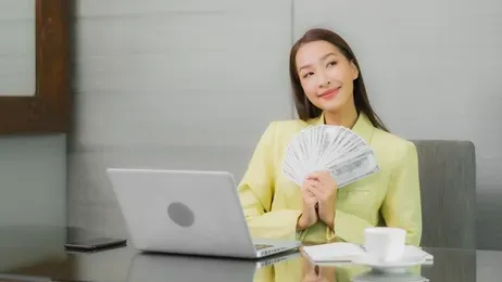 ผู้หญิงถือเงินนั่งหน้าแล็บท็อป