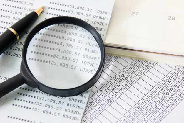 สเตทเม้นธนาคารพร้อมสมุดบัญชีที่โชว์ตัวเลขมีแว่นขยายวางอยู่ด้านบนและปากกา