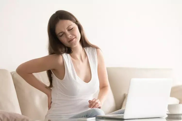 ผู้หญิงมีอาการปวดหลังขณะนั่งทำงานบนโซฟา