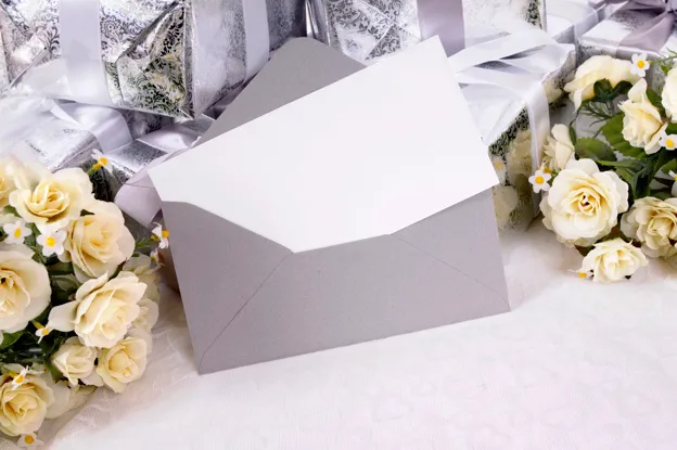 ซองสีเทาและการ์ดวางอยู่กับกล่องของขวัญและดอกกุหลาบสีขาว 